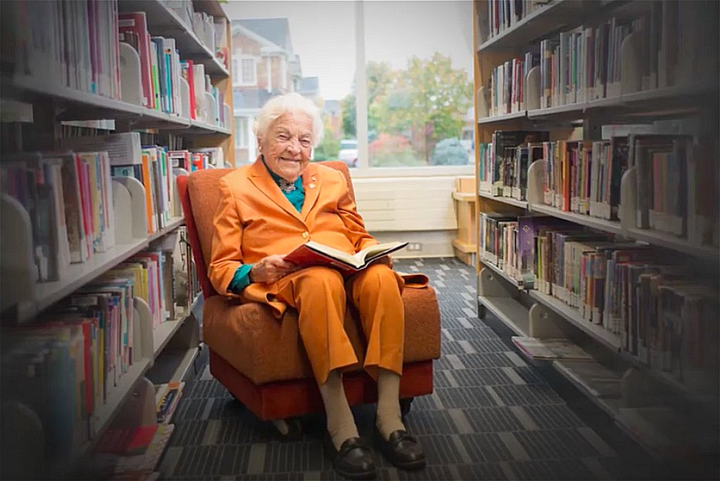 Hazel McCallion sitting with a book in Library Google image from https://capitalcurrent.ca/mccallions-100th-birthday-bash-showcases-arts-councils-smooth-transition-to-virtual-platforms-during-pandemic/